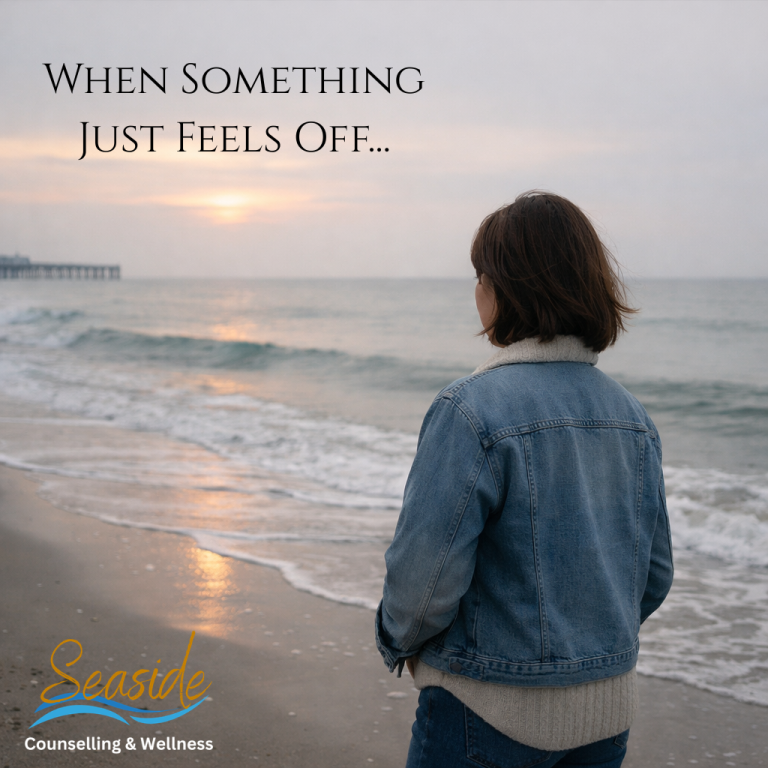 Person standing alone on a quiet beach at sunrise, looking out toward the ocean with a reflective posture, representing a subtle sense of emotional disconnection or feeling “off,” with soft muted tones and Seaside Counseling & Wellness branding overlay.